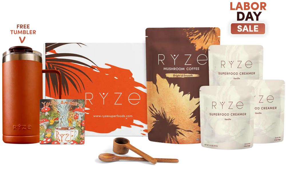 RYZE Labor Day gift set featuring a rust-orange insulated tumbler, RYZE Mushroom Coffee pouch, RYZE Superfood Creamer pouches, a branded gift box, wooden measuring cups, and a 'Free Tumbler' badge on a white background.
